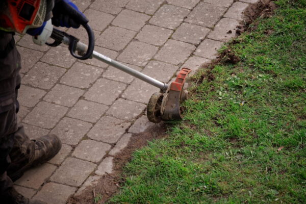 Worker uses edge trimmer at the pathway Tradie Taskforce - edging